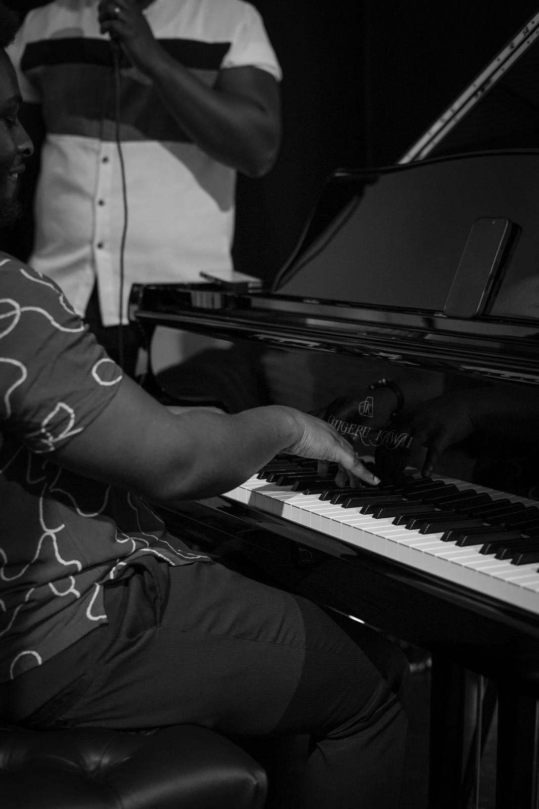 Black and white close-up of Ato Baah-Nyarkoh's hand on the keys of a Shigeru Kawai grand piano.