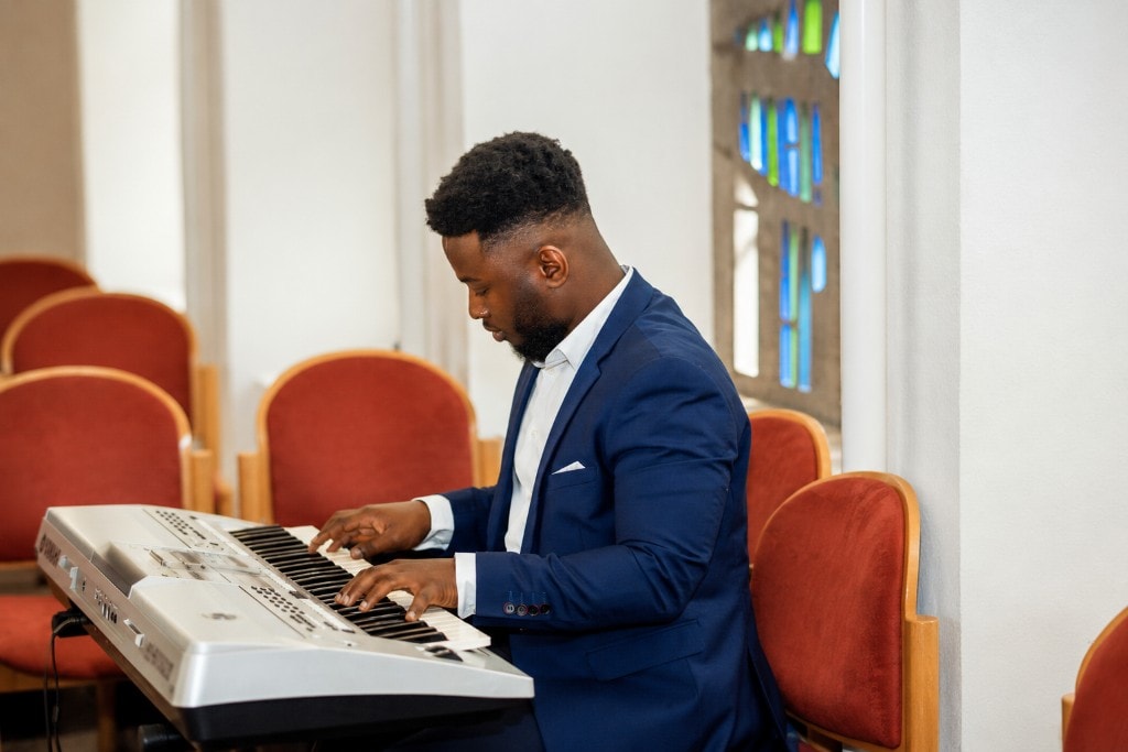 Ato Baah-Nyarkoh playing keyboard during a service in a stained-glass sanctuary.