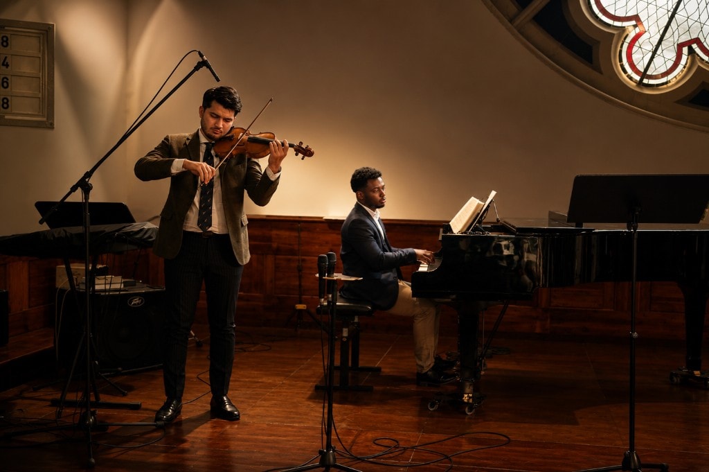 Ato Baah-Nyarkoh accompanying a violinist on stage in a concert hall.